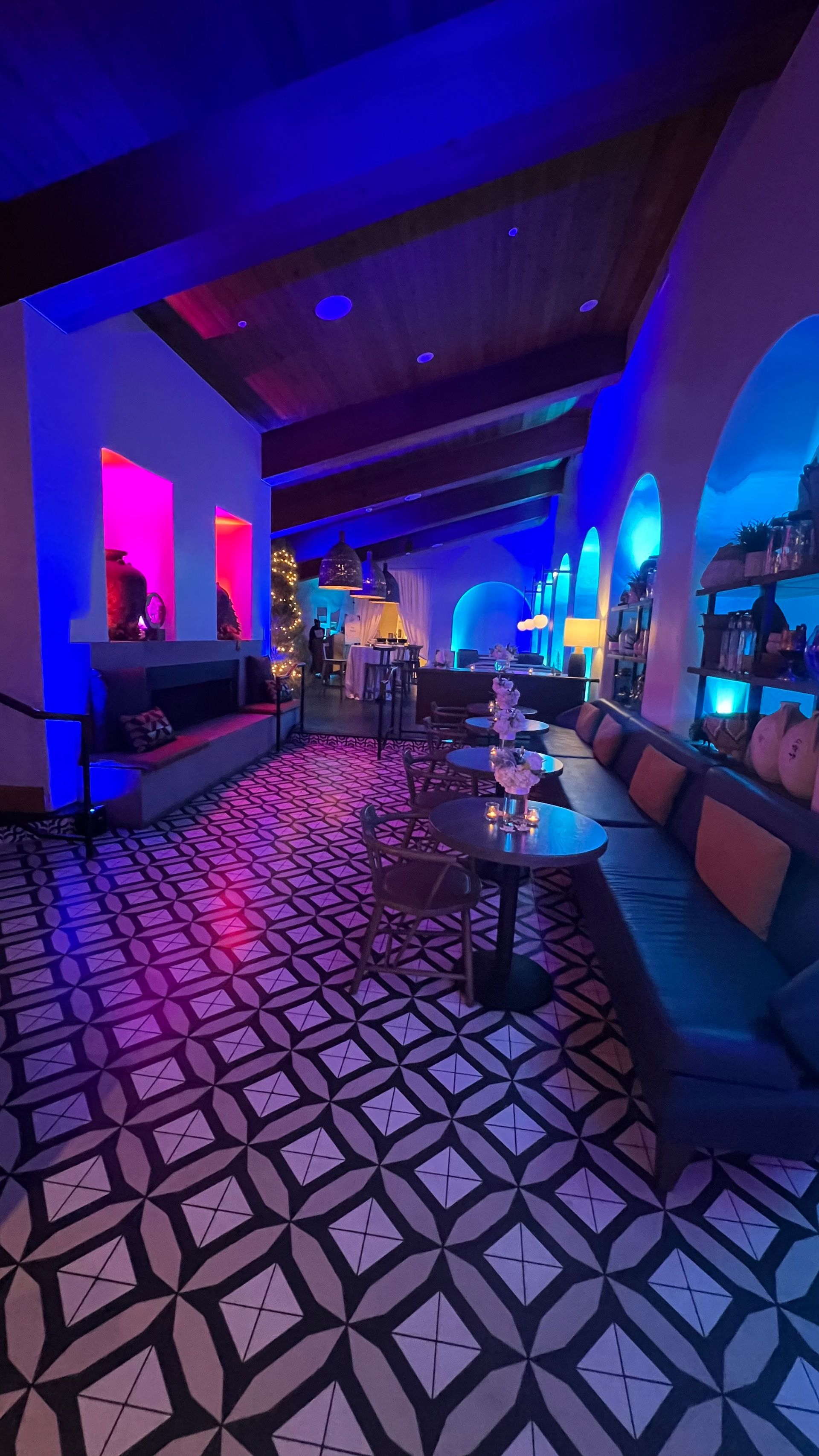 Interior with patterned floor, blue and pink lighting, seating areas, bar.