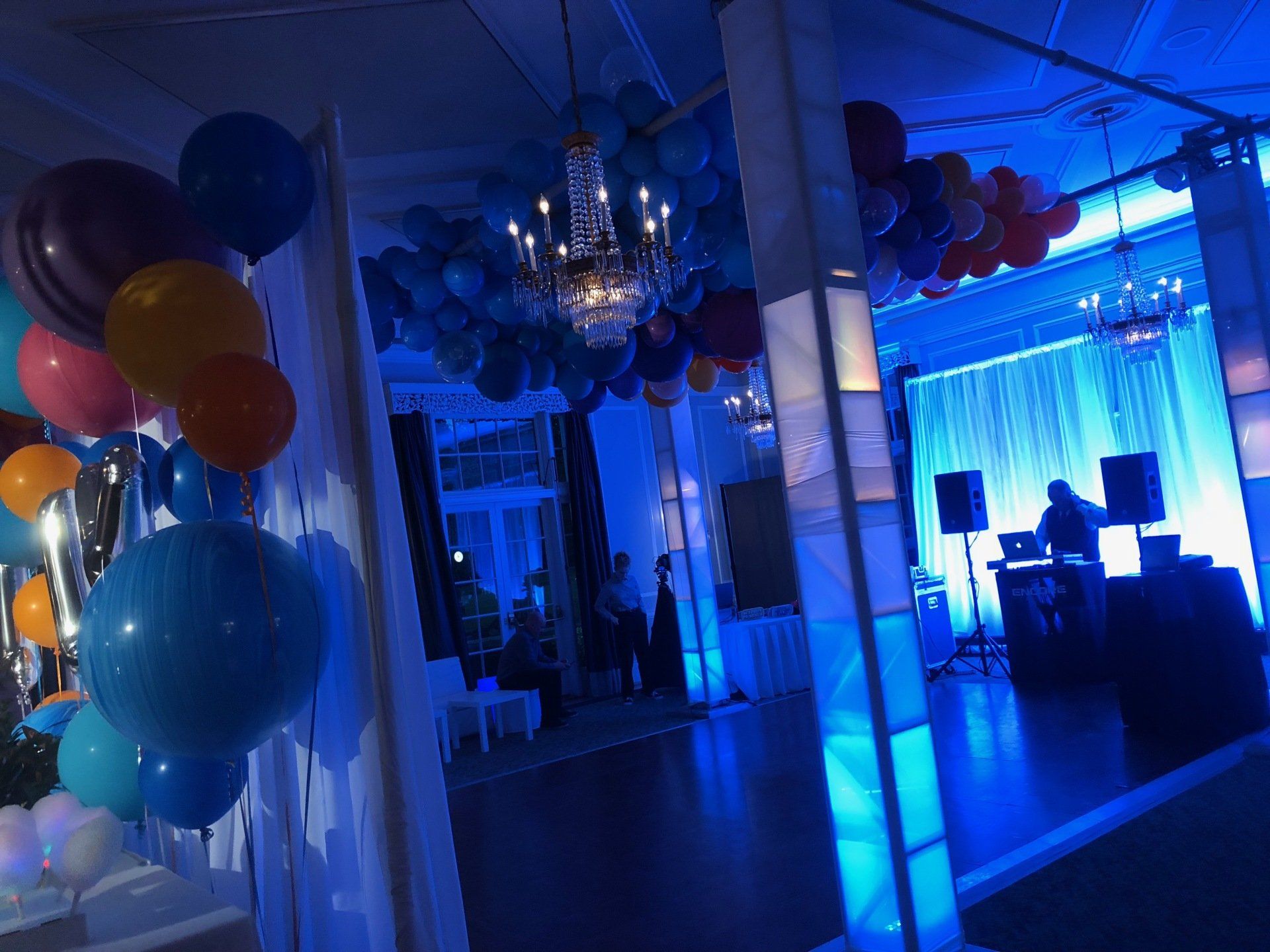 Party room with blue lighting, balloons, and a DJ.