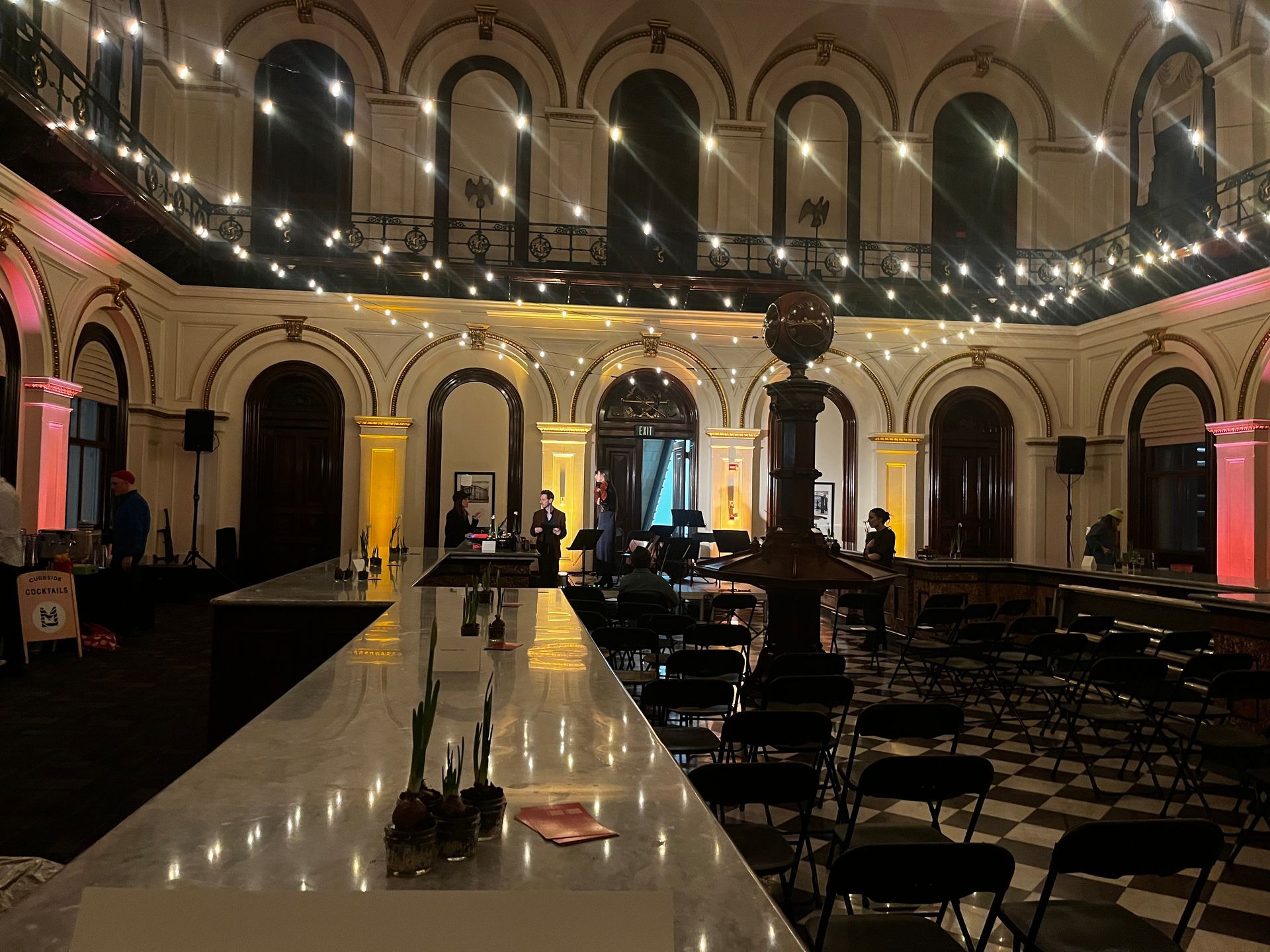 A well-lit bar with a long counter and many seats in an elegant, indoor event space.