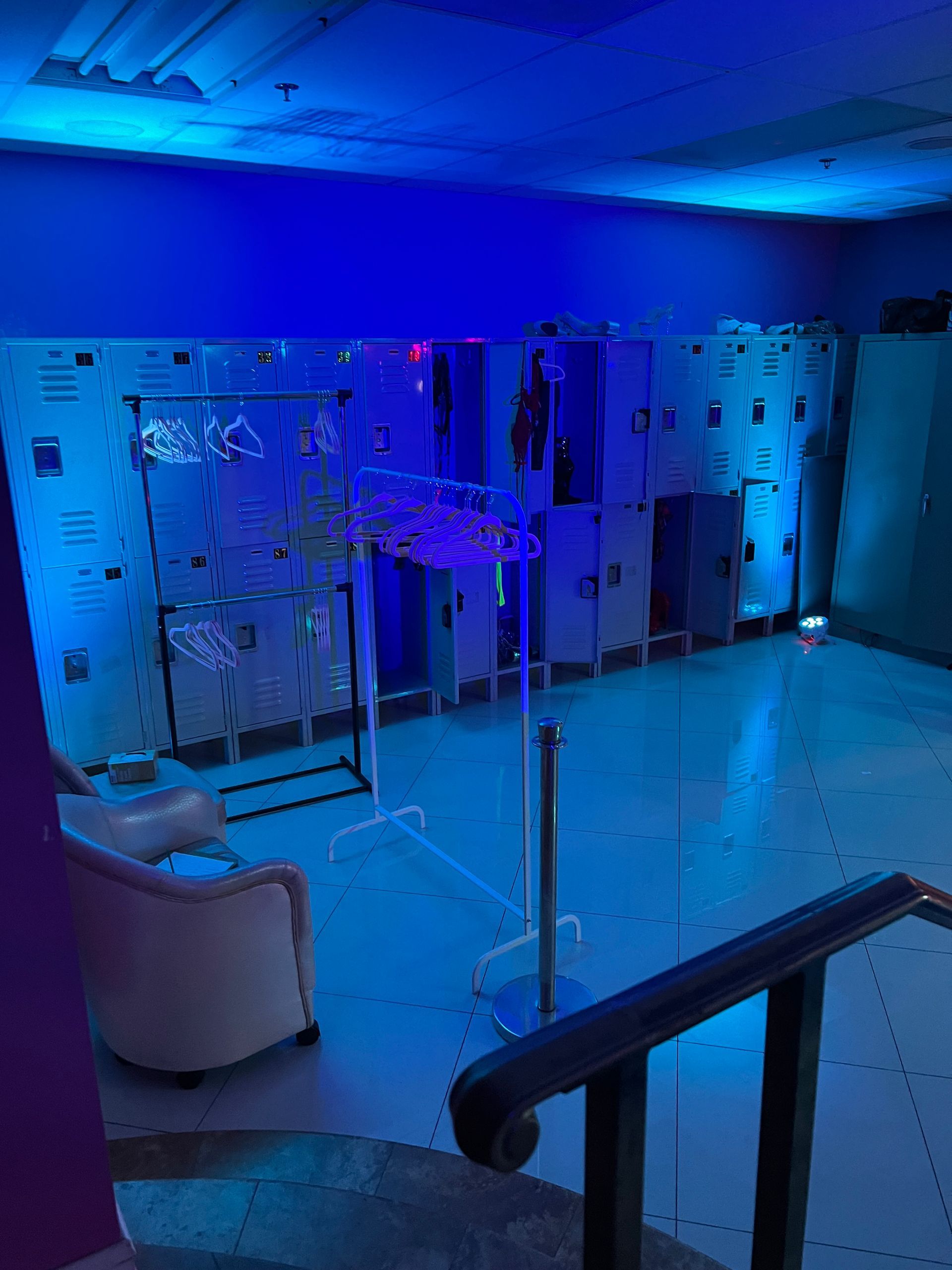 Room with lockers and seating, illuminated by blue lights.
