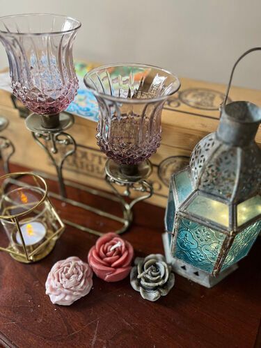 Candle holders and flower candles on a wooden table, with a teal lantern and vintage-style candle holder.