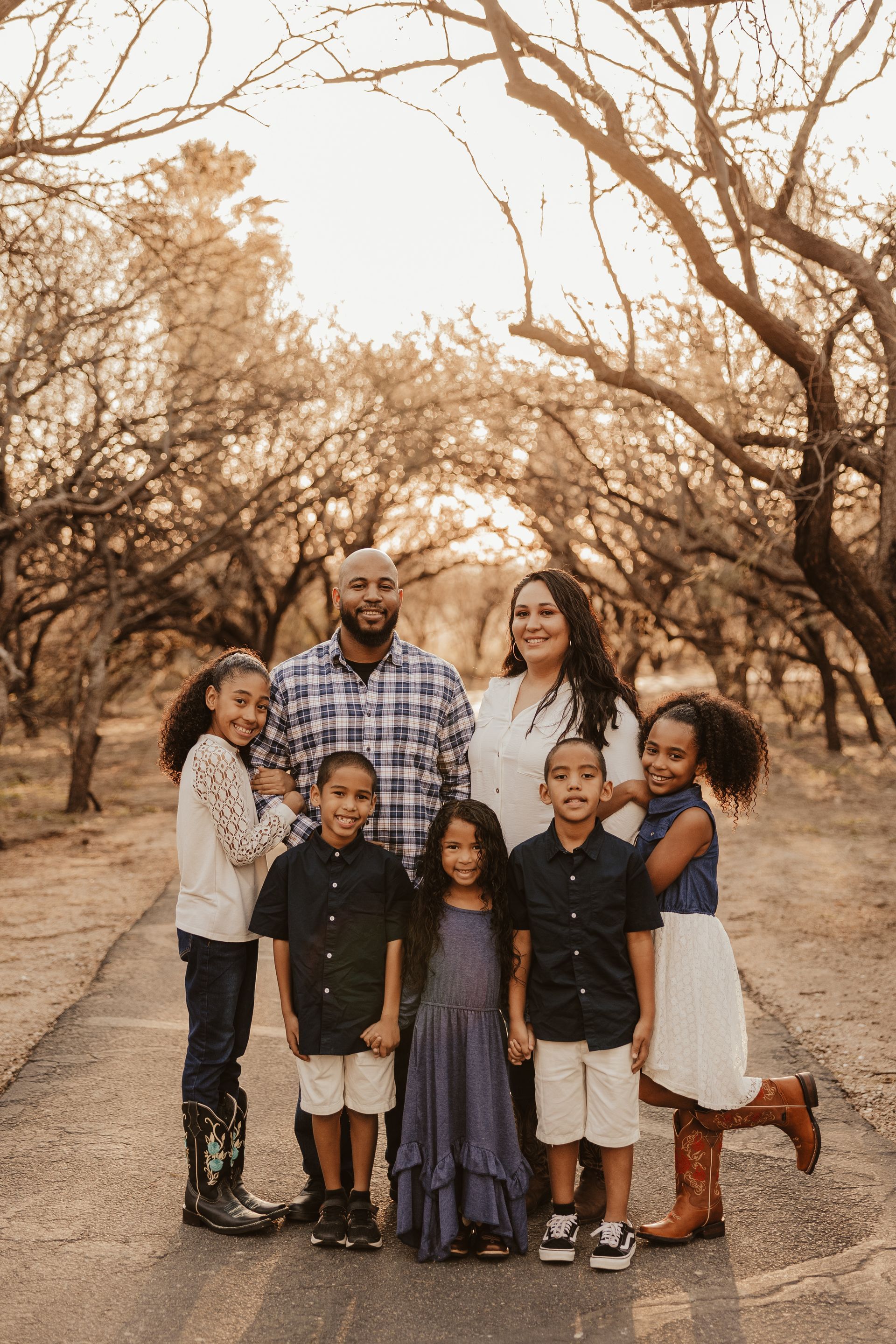 Family of seven poses on a path lined with trees; golden light illuminates the scene.