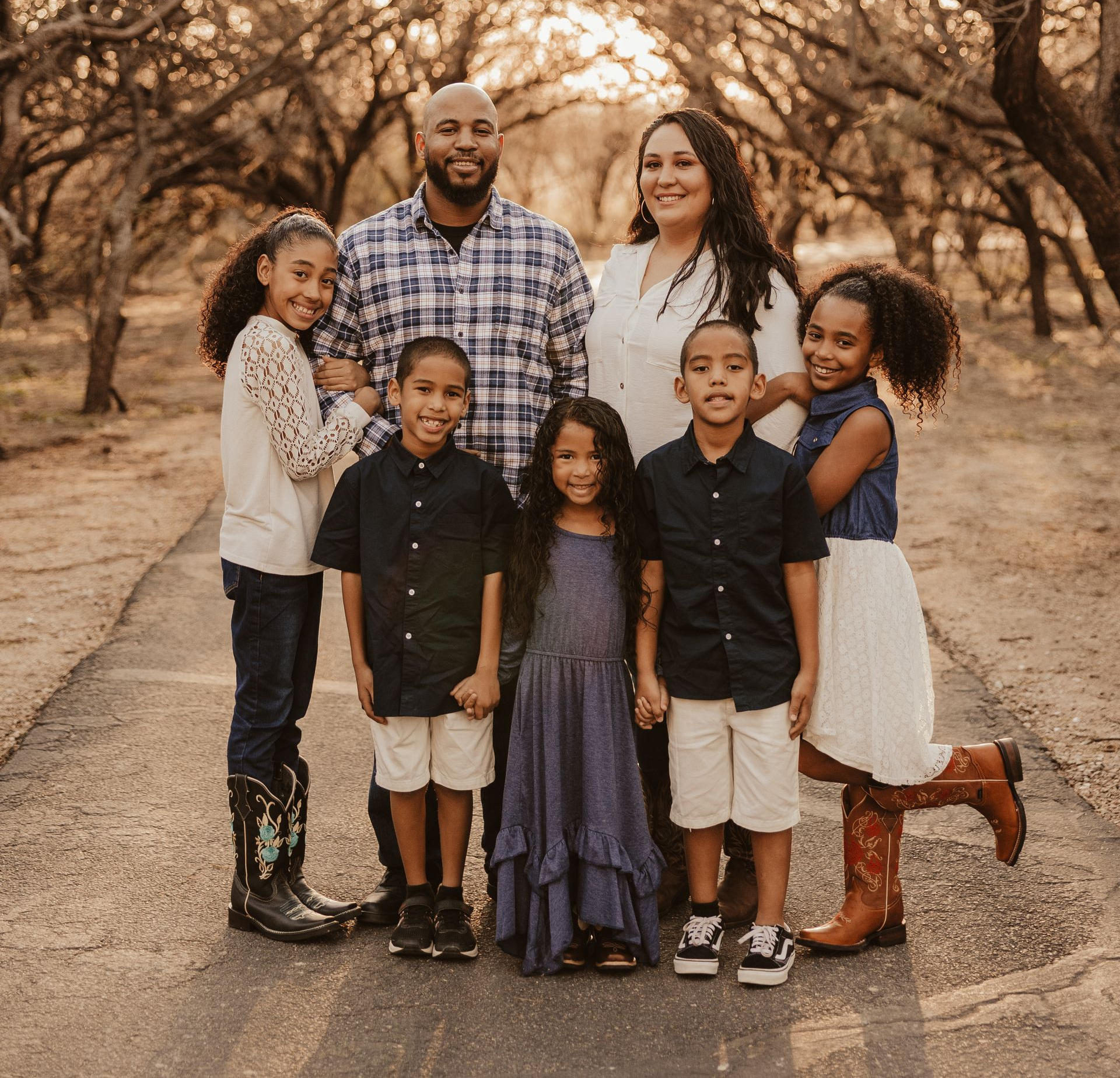 Family of seven poses on a path lined with trees; golden light illuminates the scene.