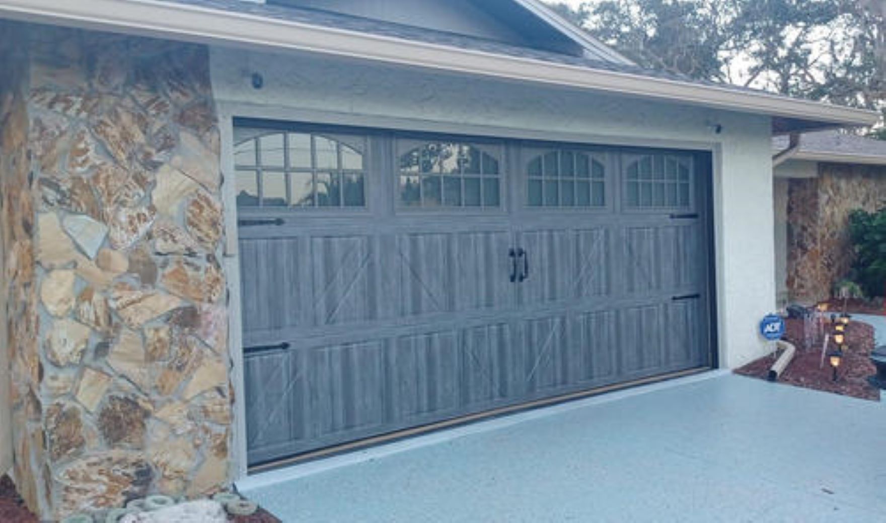 Gray garage door with window panels and stone accent.