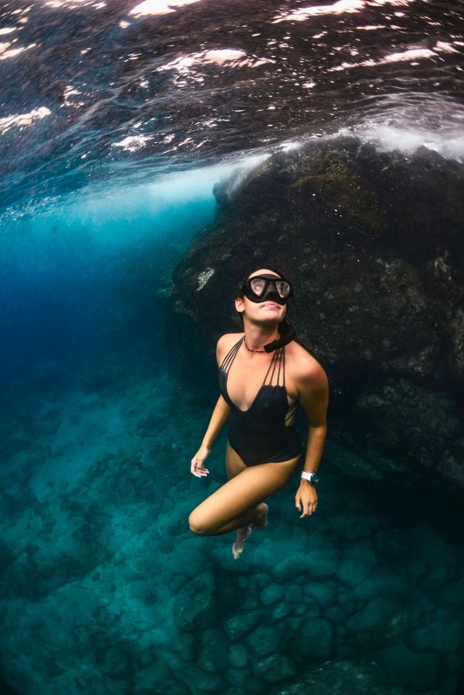 A woman in a black swimsuit is freediving underwater in the ocean.