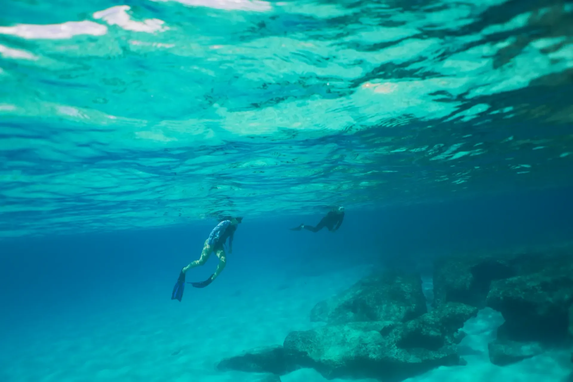 A couple of people are freediving in the ocean near a coral reef.