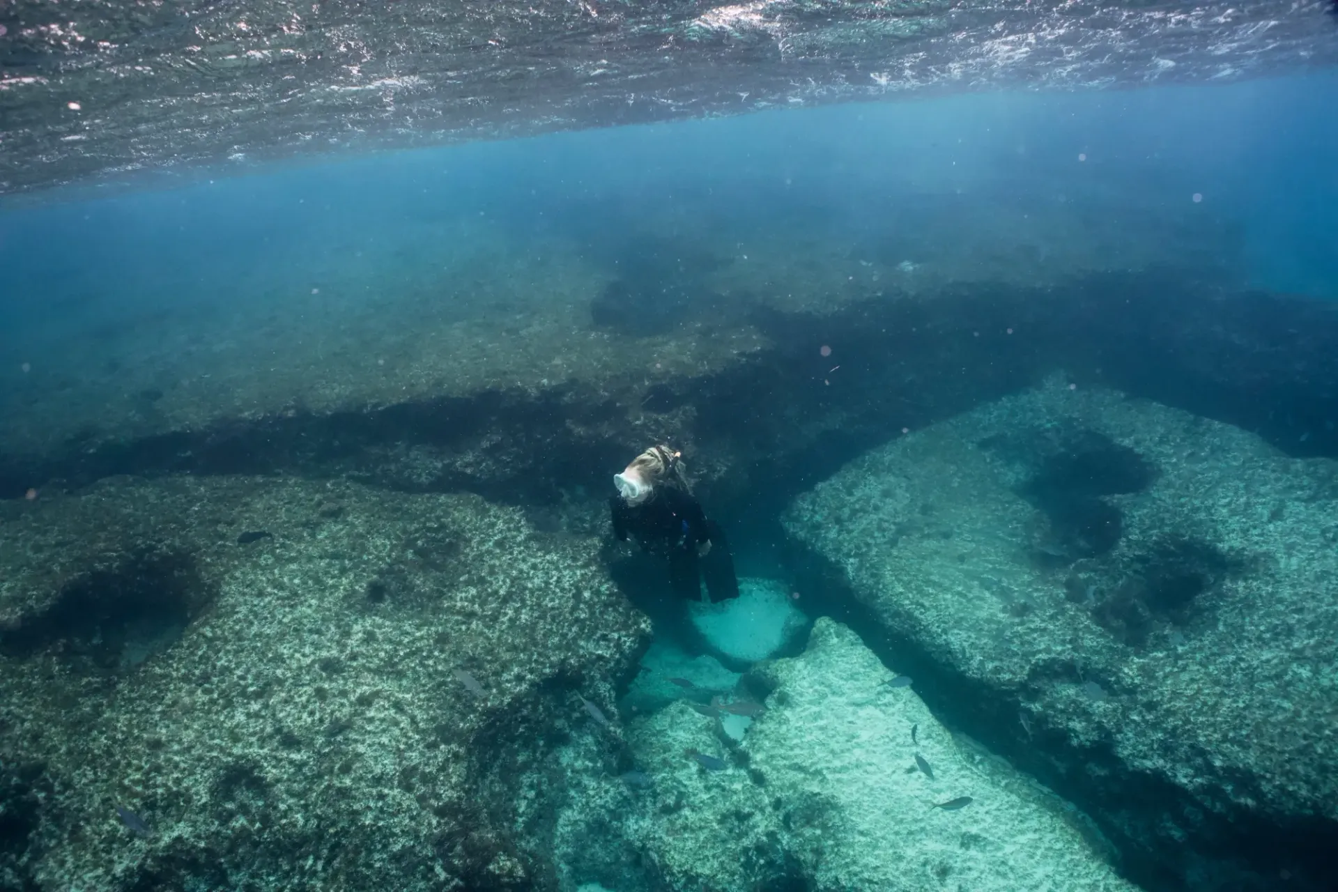 A freediver is swimming in the ocean near a rocky reef.