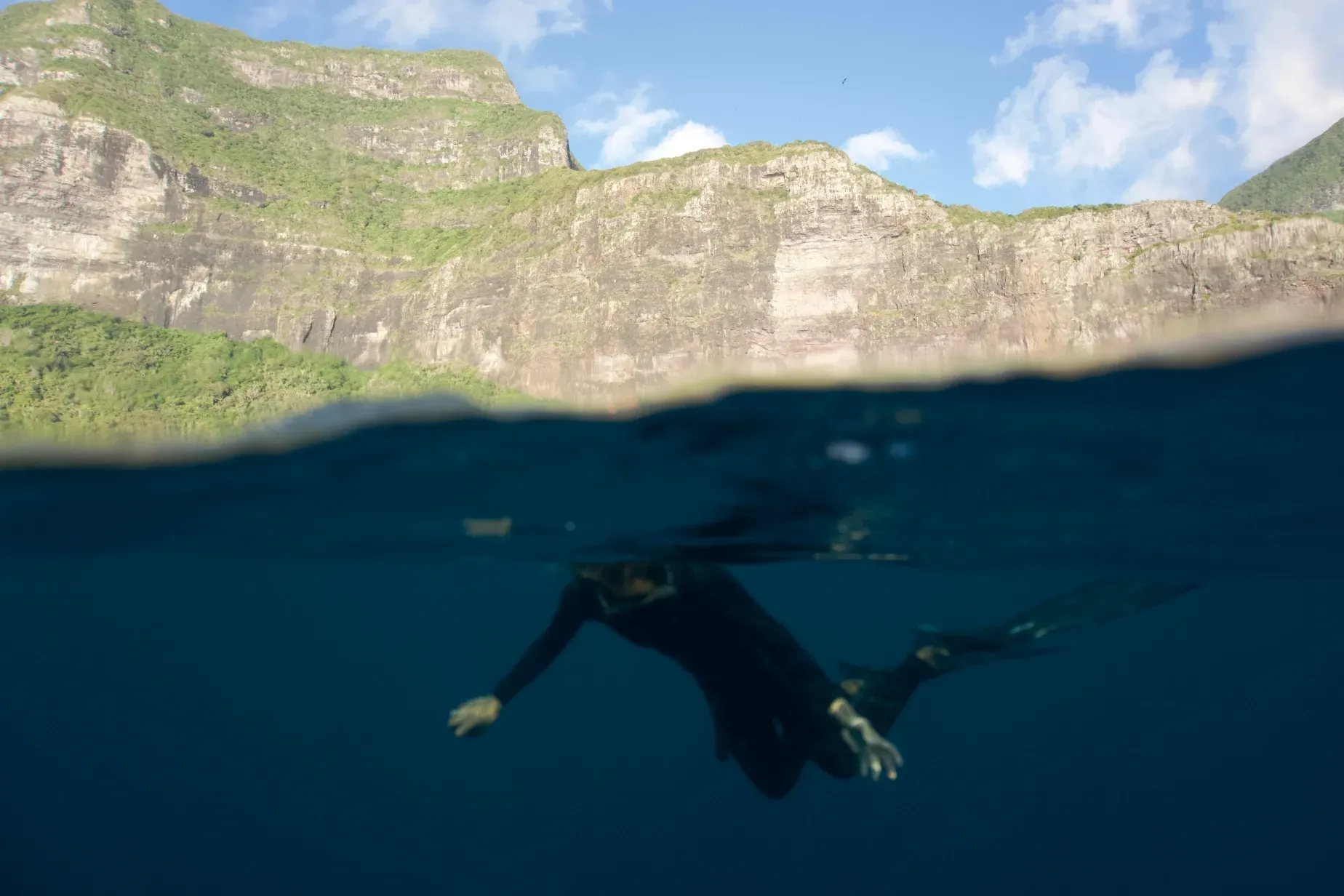 A person is freediving in the ocean with mountains in the background.