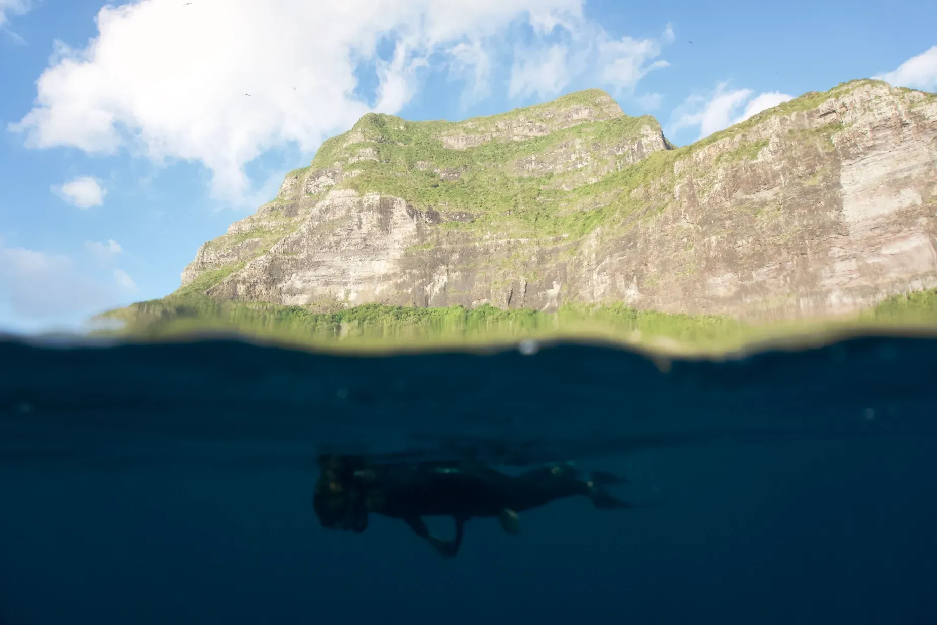 A person is freediving in the ocean with a mountain in the background.