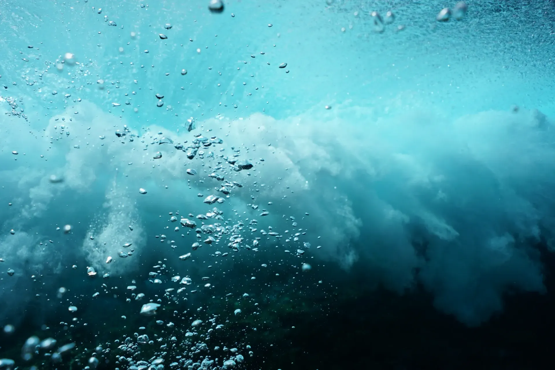A wave is breaking in the ocean with bubbles coming out of it.