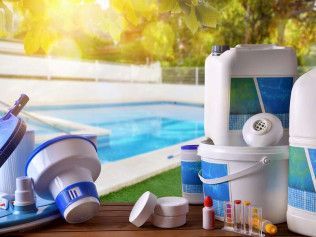 A table topped with a variety of swimming pool supplies in front of a swimming pool.