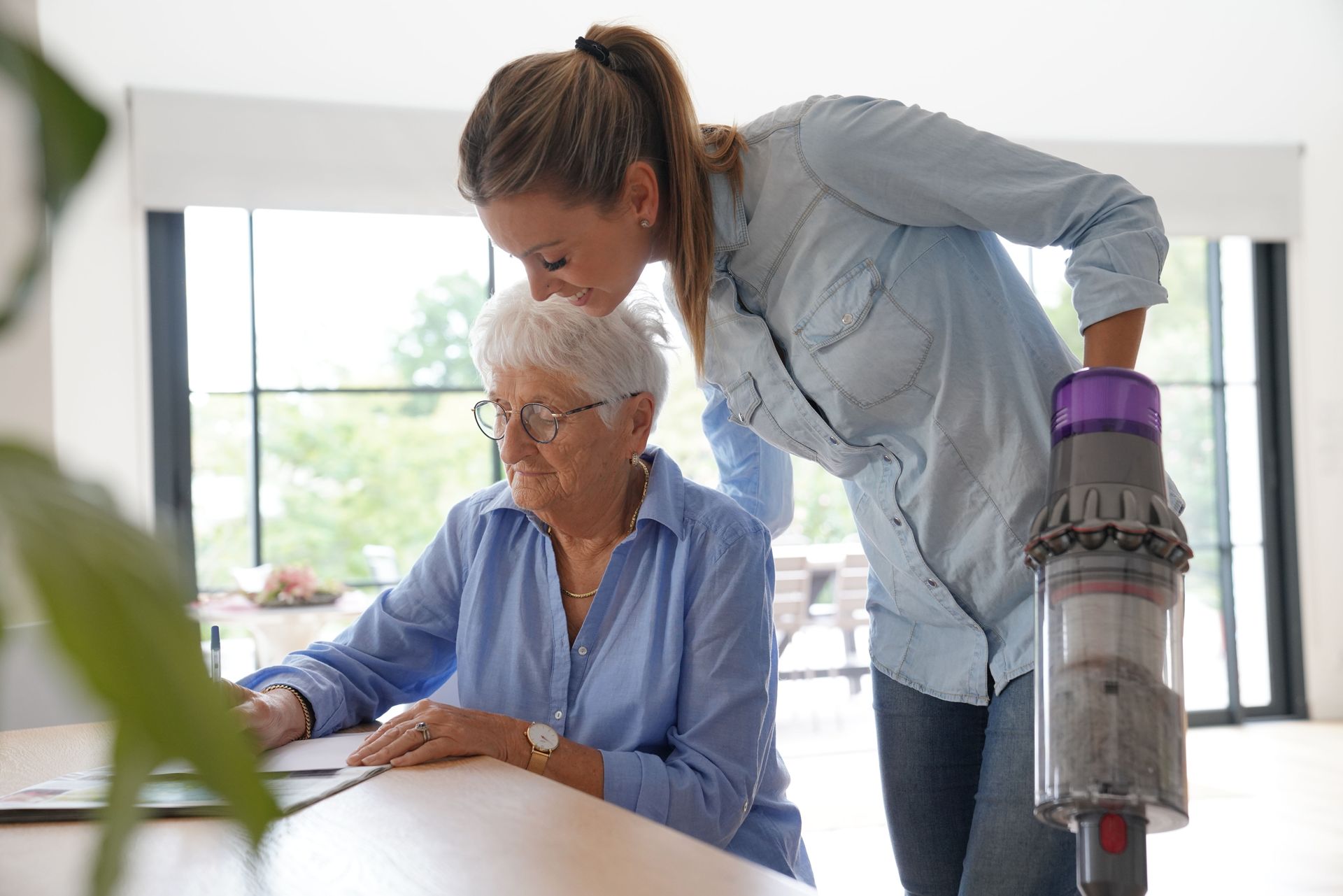 A woman is standing next to an older woman sitting at a table.