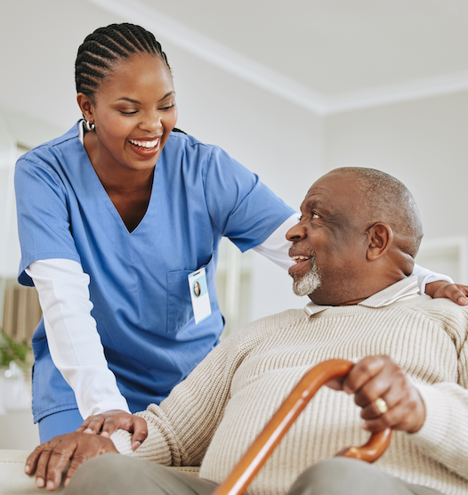 A woman in a blue scrub is talking to an older man with a cane