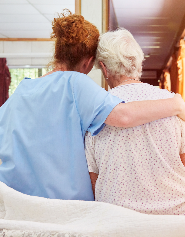 A nurse is hugging an elderly woman in a hospital bed.