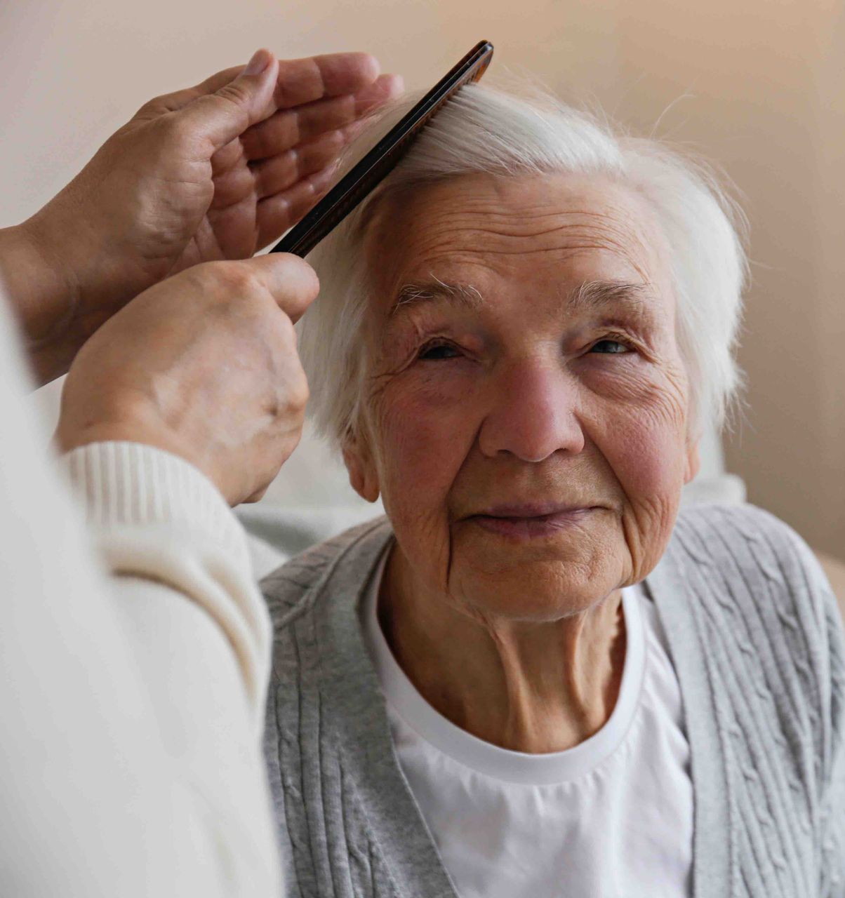 An elderly woman is getting her hair combed by a woman.