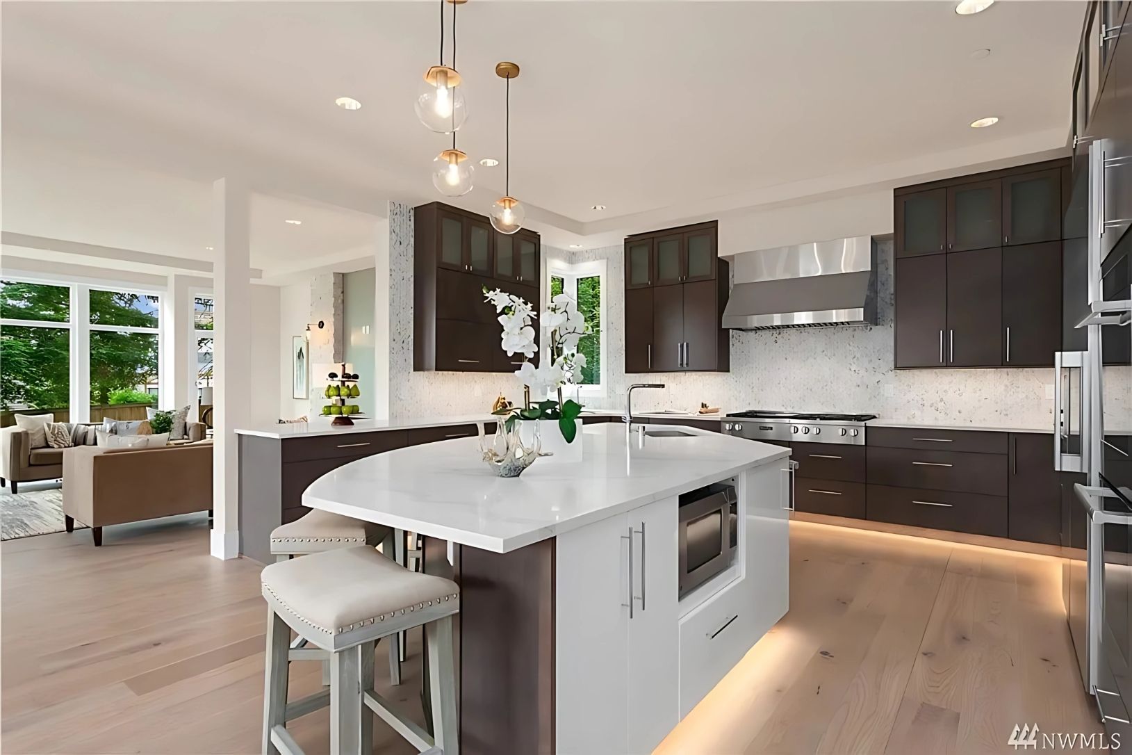 Modern kitchen with dark wood cabinets, white island with seating, and light-colored wood floors.