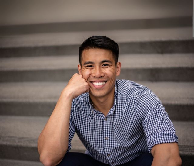 A man in a plaid shirt is sitting on a set of stairs and smiling.