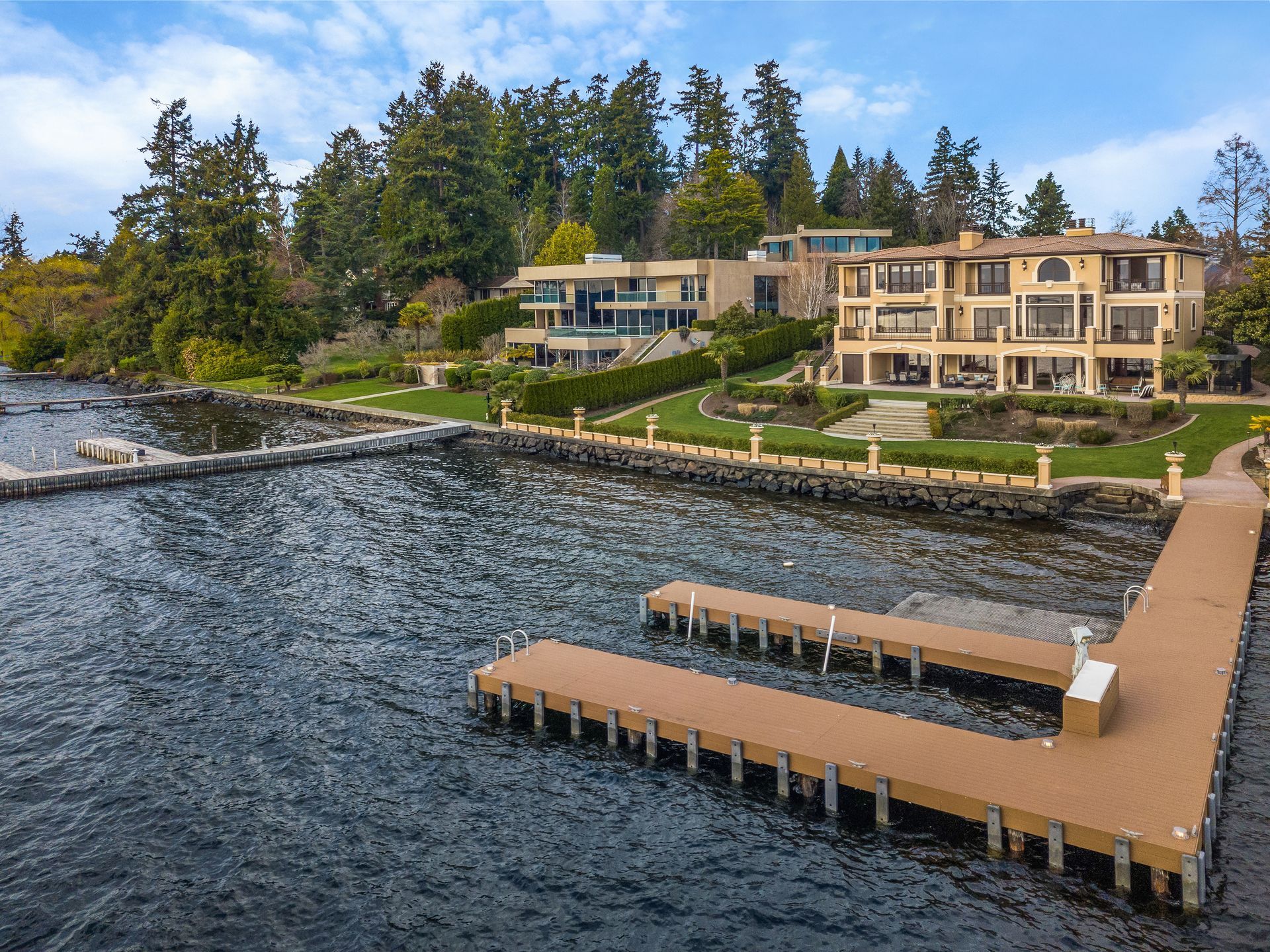 A large house sits on the shore of a lake next to a dock.