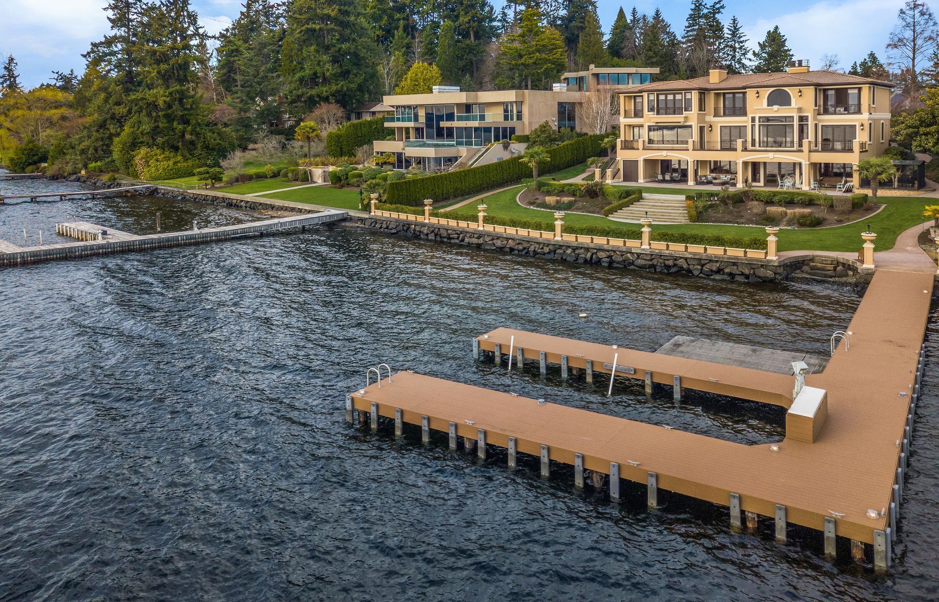 A large house sits on the shore of a lake next to a dock.