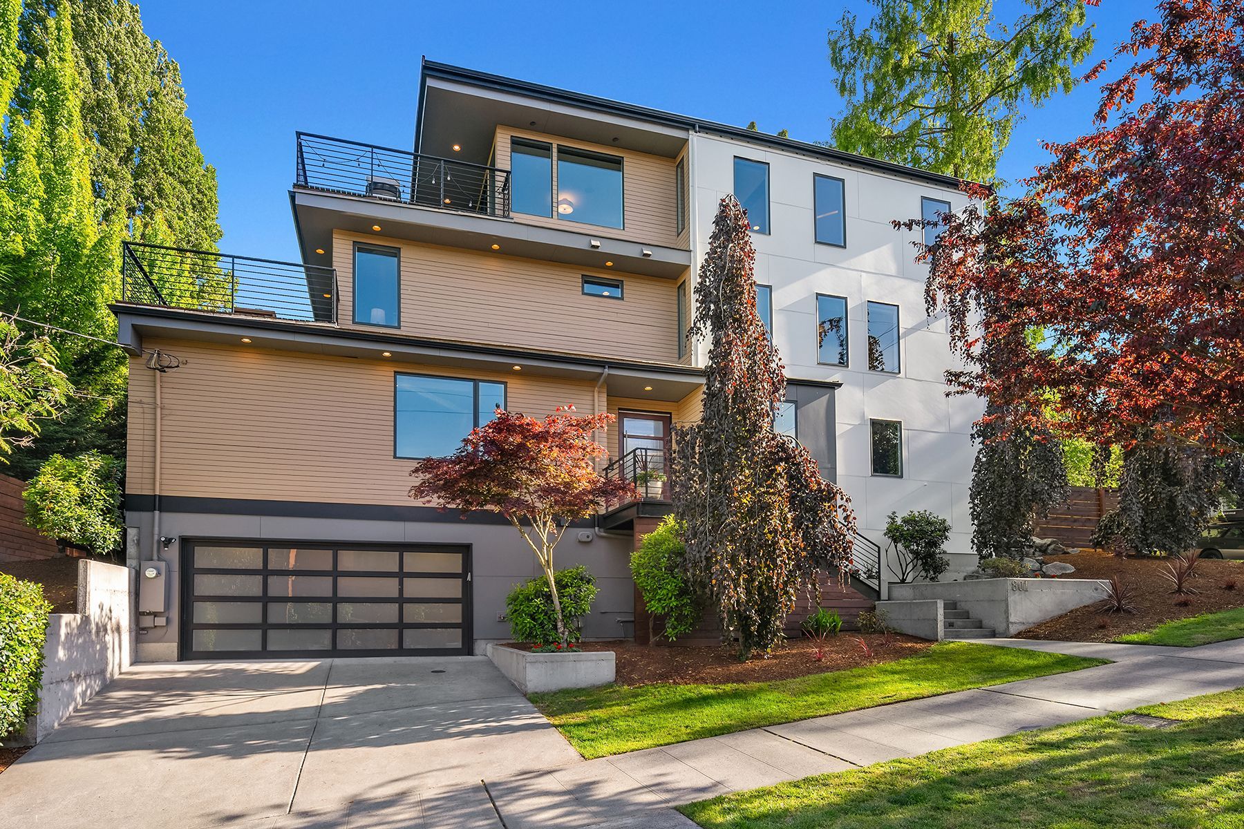 A modern house with a large garage and a balcony surrounded by trees.
