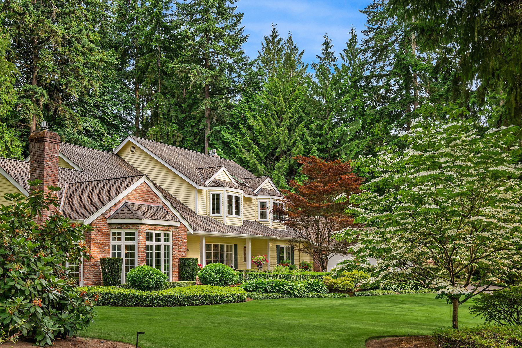 A large house with a large lawn in front of it is surrounded by trees.
