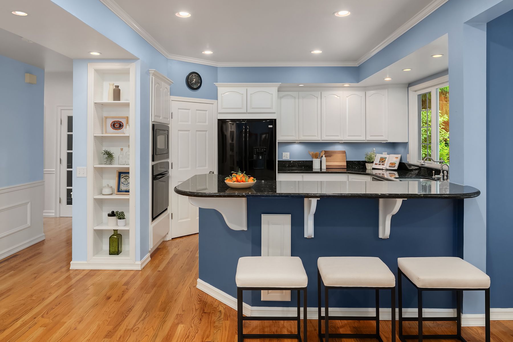 A kitchen with blue walls , white cabinets , and a black refrigerator.