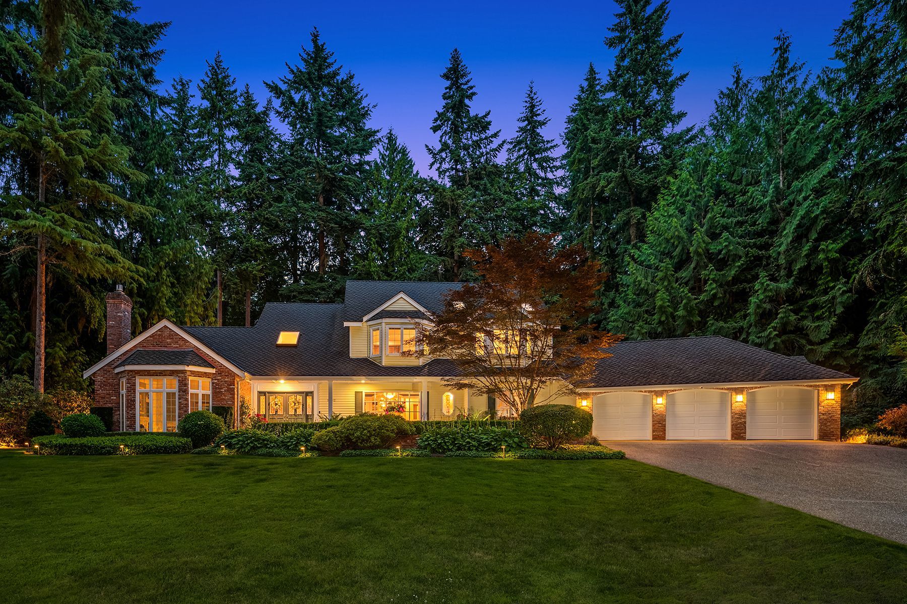 A large house is lit up at night with trees in the background