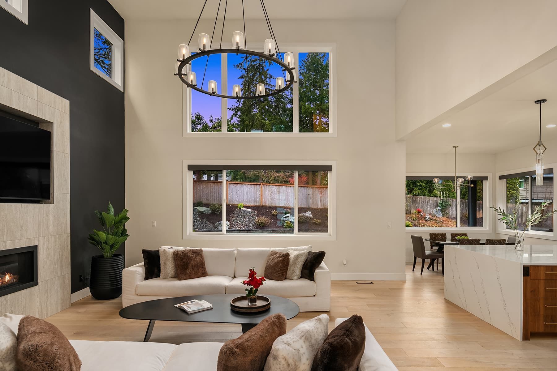 Spacious living room with a white couch, fireplace, large windows, and a chandelier.
