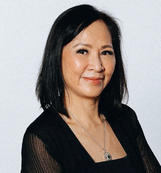 A woman wearing a black shirt and a necklace is smiling for the camera.