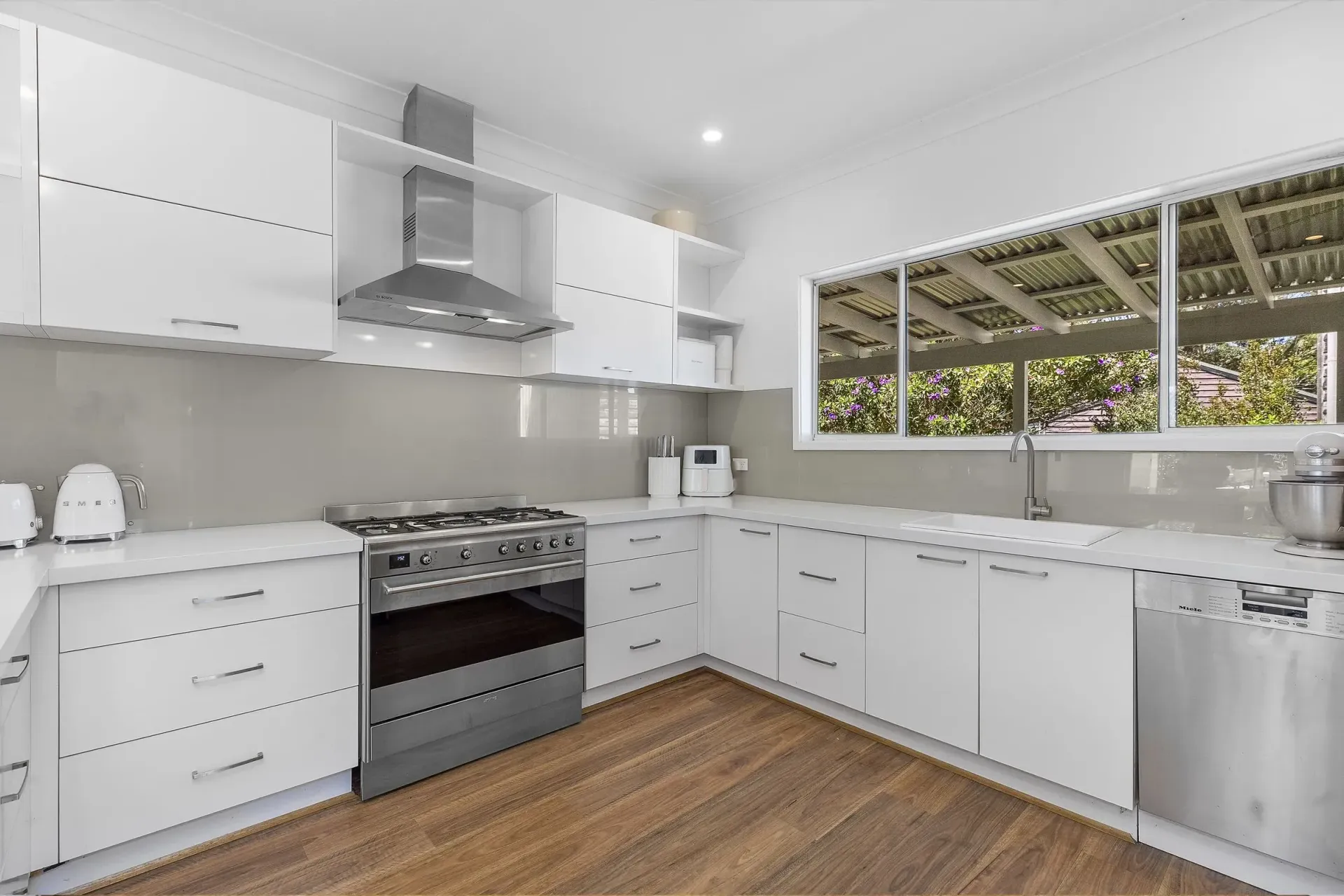 After photo of White modern kitchen with stainless steel appliances, white cabinets, and a window - Wards Kitchens In Central Coast, NSW
