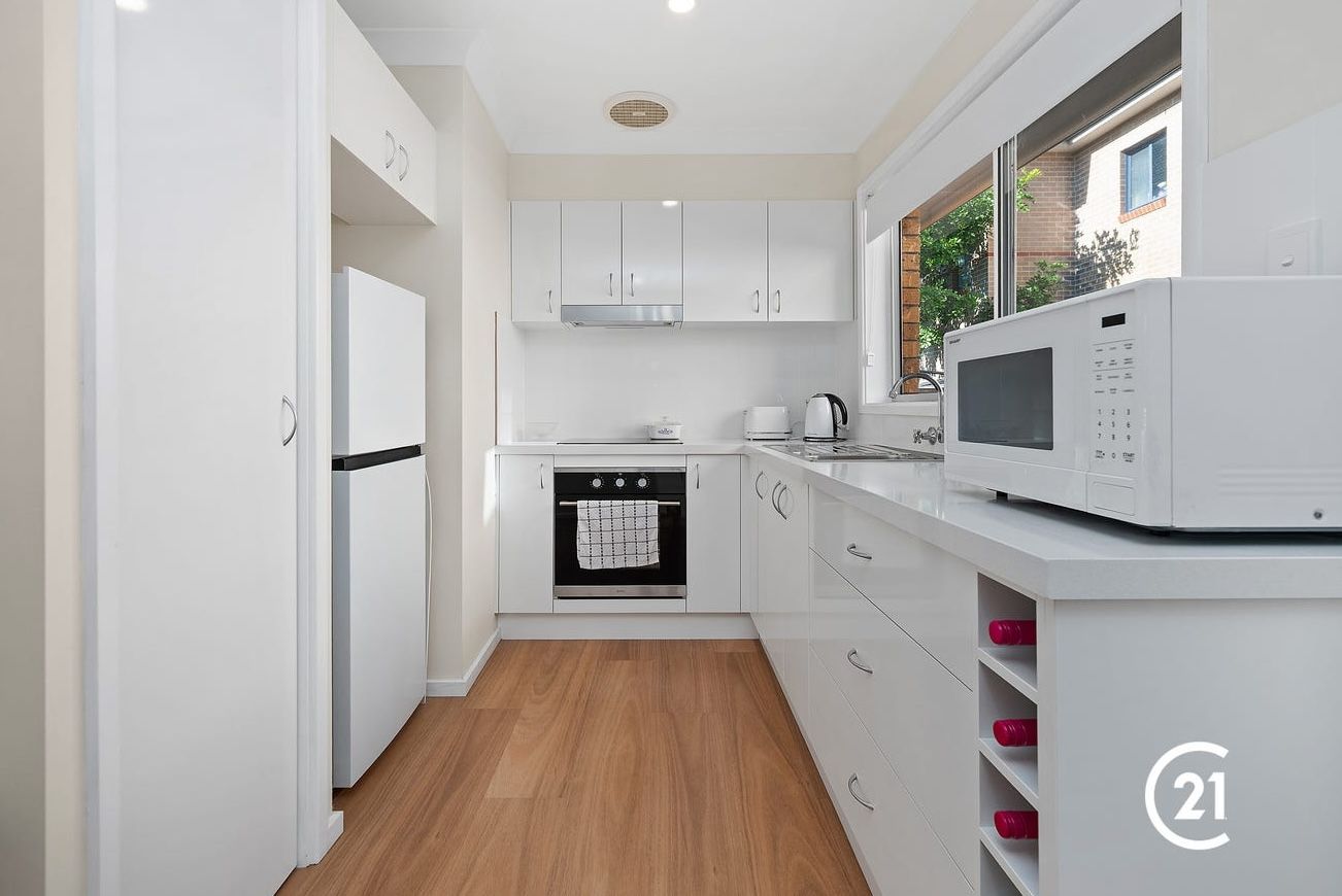 White kitchen with cabinets, appliances, and wooden flooring.