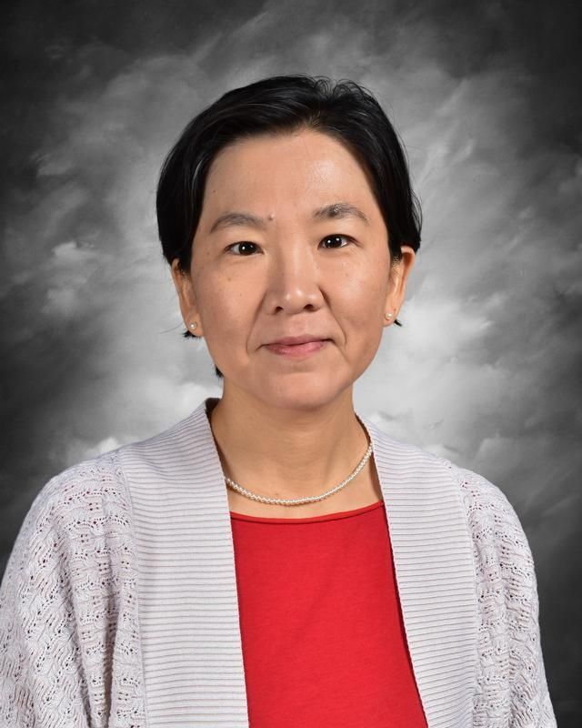 A woman in a red sweater and black vest is standing in front of a blue background.