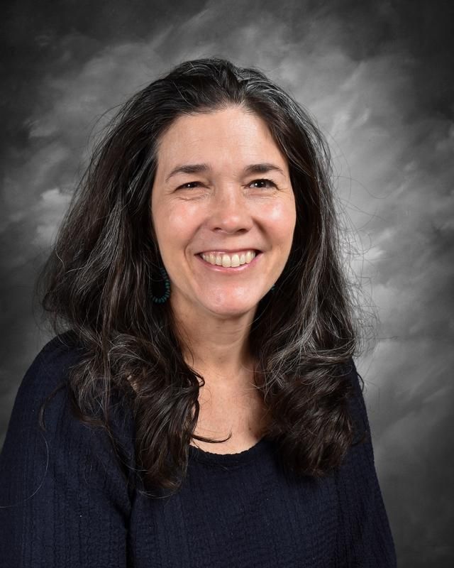A woman in a black and white striped shirt is smiling in front of a blue background.