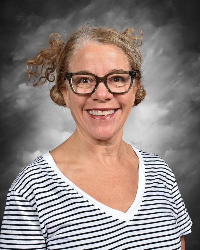 A woman wearing glasses and a black jacket is smiling for a picture.