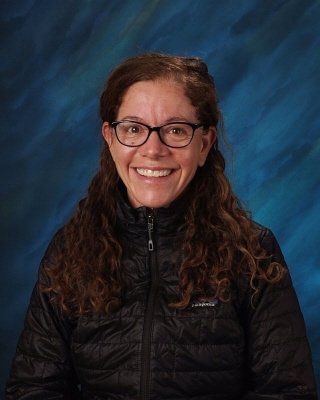 A woman wearing glasses and a black jacket is smiling for a picture.