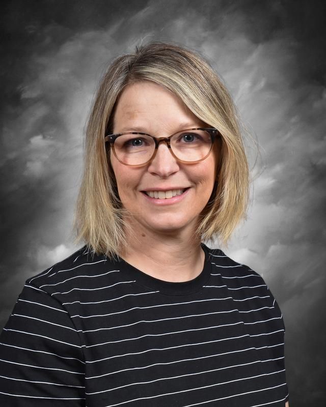 A woman wearing glasses and a pink scarf is smiling for the camera.