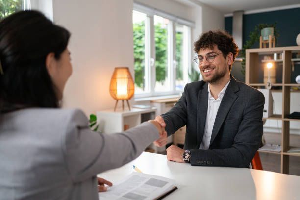 Man and woman shaking hands at a table, smiling in an office setting.
