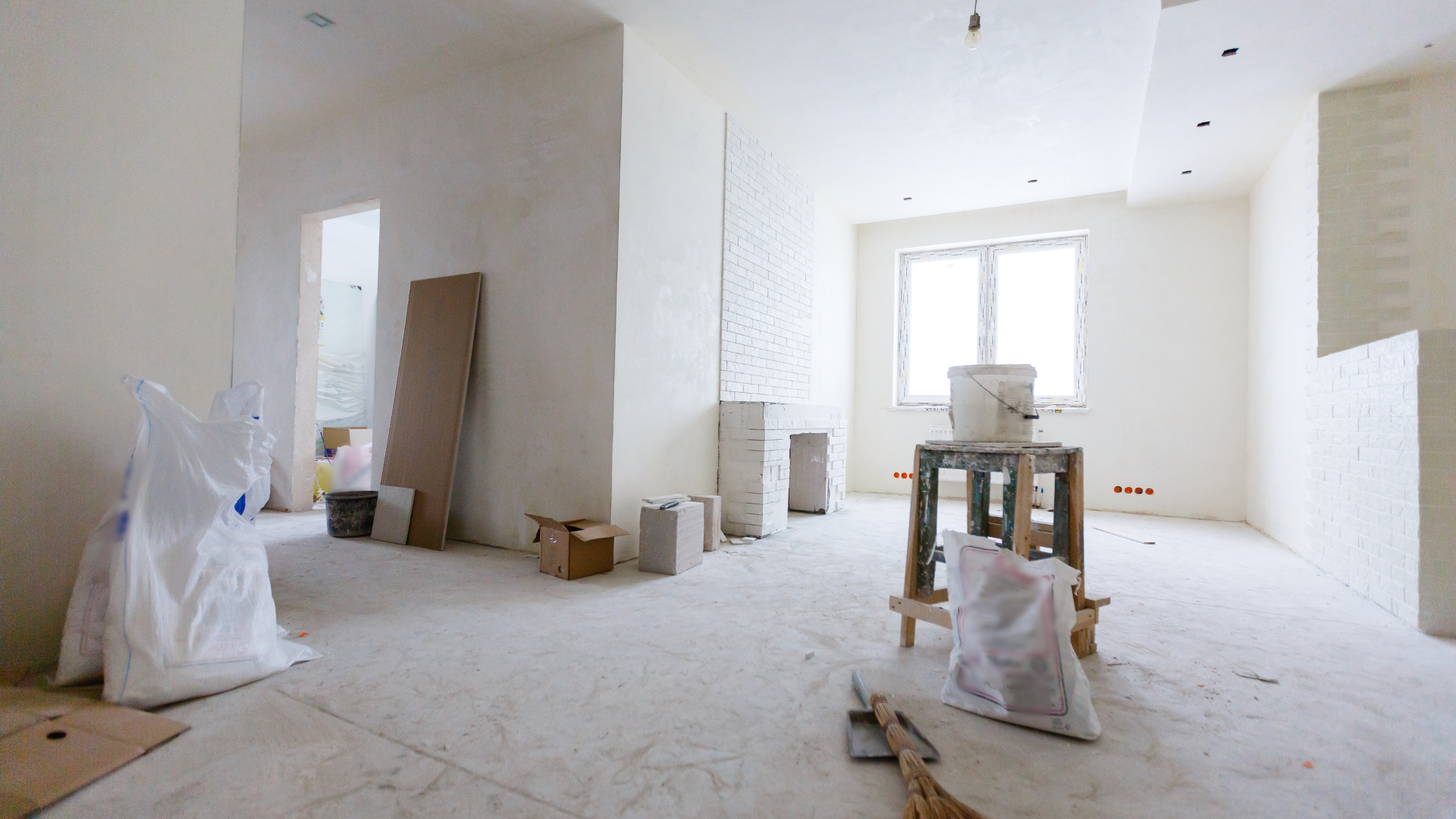 Interior of an unfurnished room under renovation with white walls, a workbench, and construction debris on the floor.