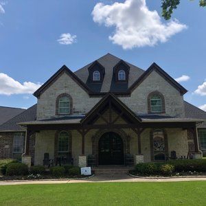 A large brick house with a black roof is sitting on top of a lush green lawn.