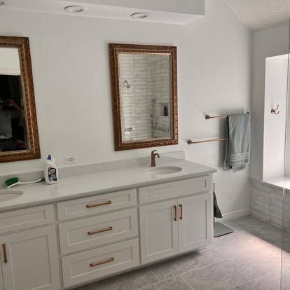 A bathroom with white cabinets , a sink , a mirror and a bathtub.