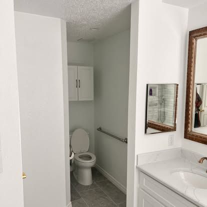 A bathroom with a toilet , sink and mirror.