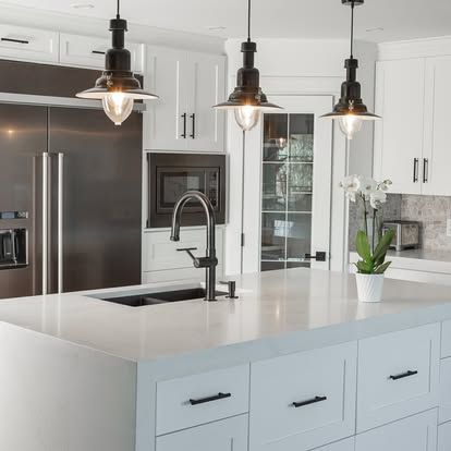 A kitchen with white cabinets , stainless steel appliances , a sink and a refrigerator.
