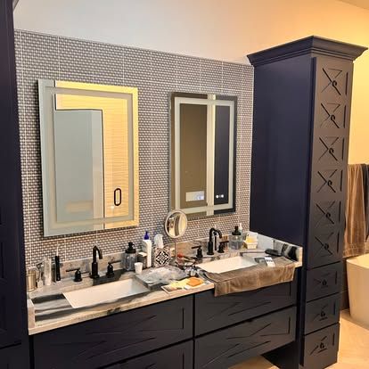 A bathroom with two sinks , two mirrors , and a tall cabinet.