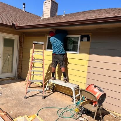A man is standing on a ladder painting the side of a house.