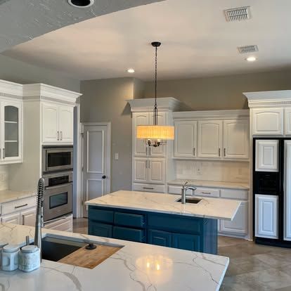 A kitchen with white cabinets , a blue island , a sink , and a refrigerator.