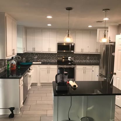A kitchen with white cabinets , black counter tops , stainless steel appliances and a large island.