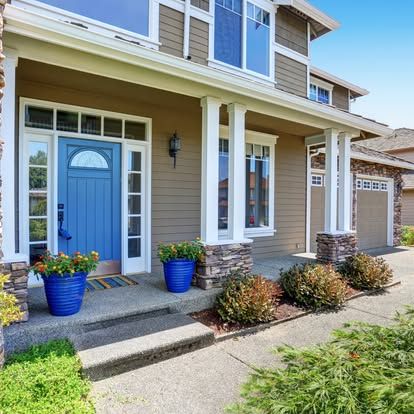 A house with a blue door and blue potted plants on the porch.