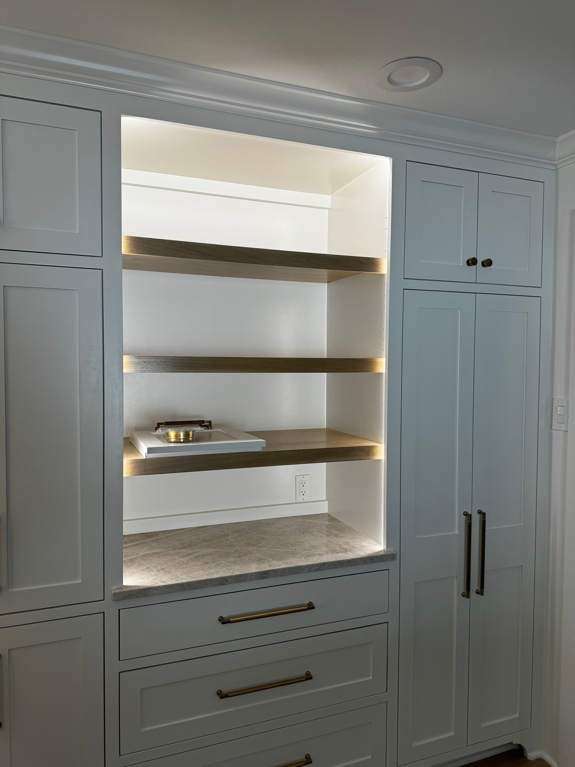 Built-in white cabinet with open shelves and drawers, lit from above, in a modern room