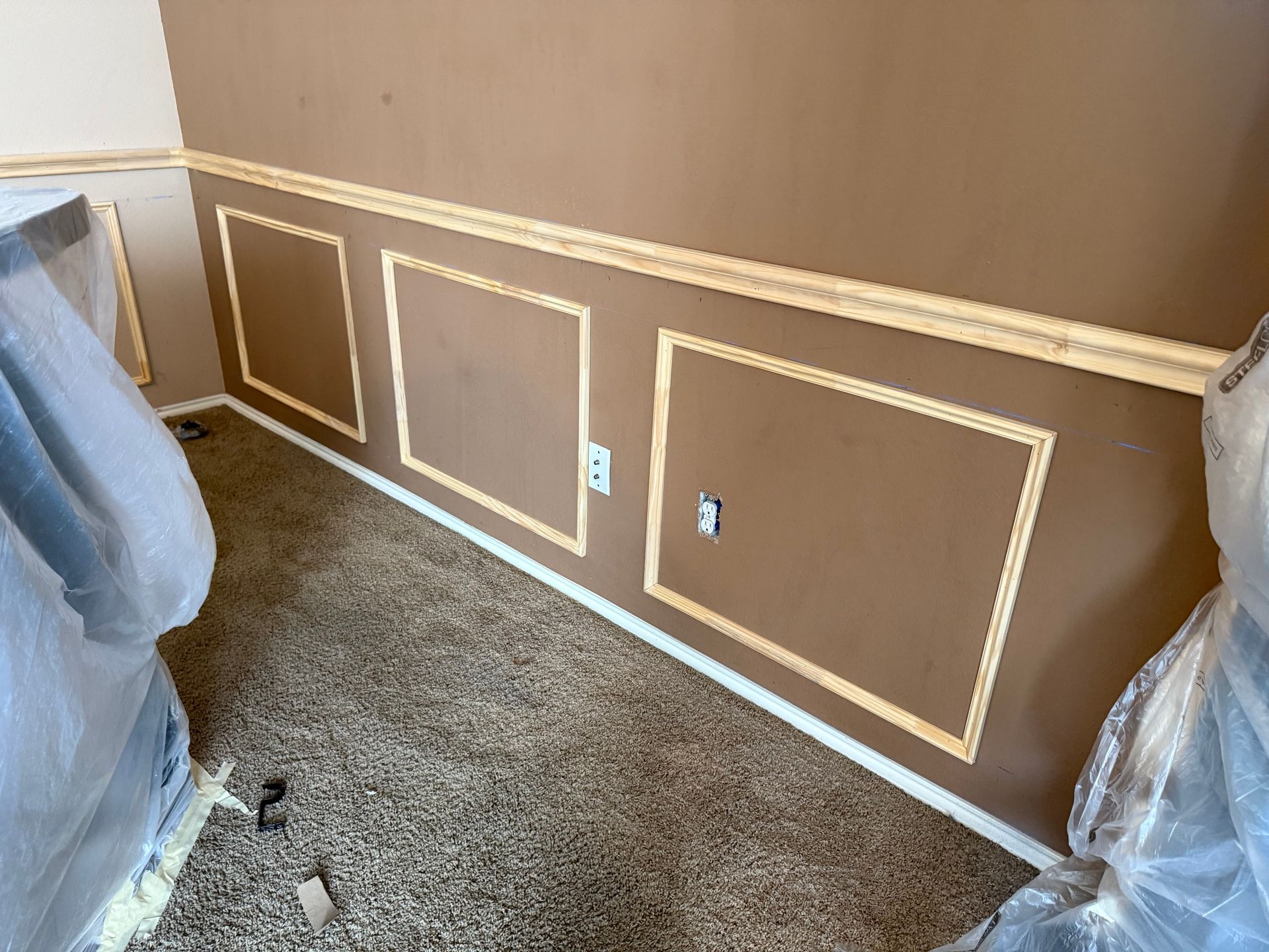 A room with brown walls and white trim is being painted.