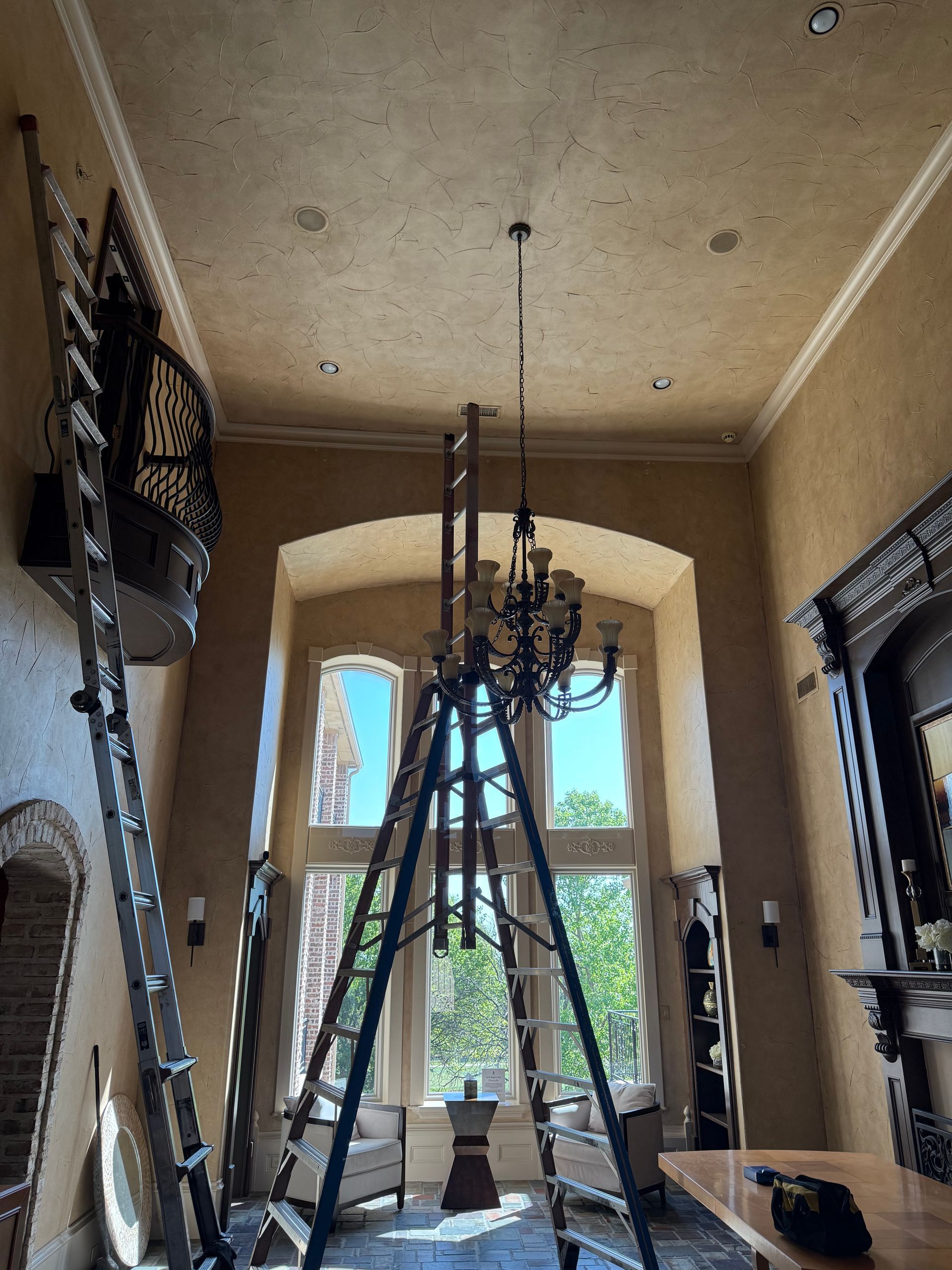 A living room with a ladder and a chandelier hanging from the ceiling.
